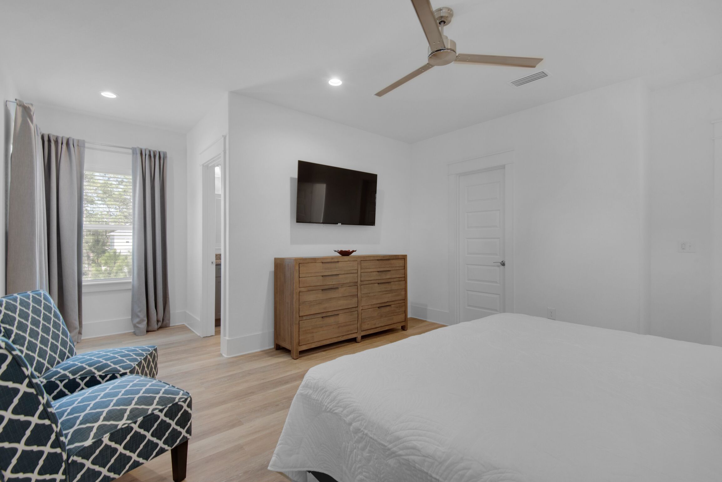 A bedroom with a bed, a wooden dresser, a television, and a ceiling fan.