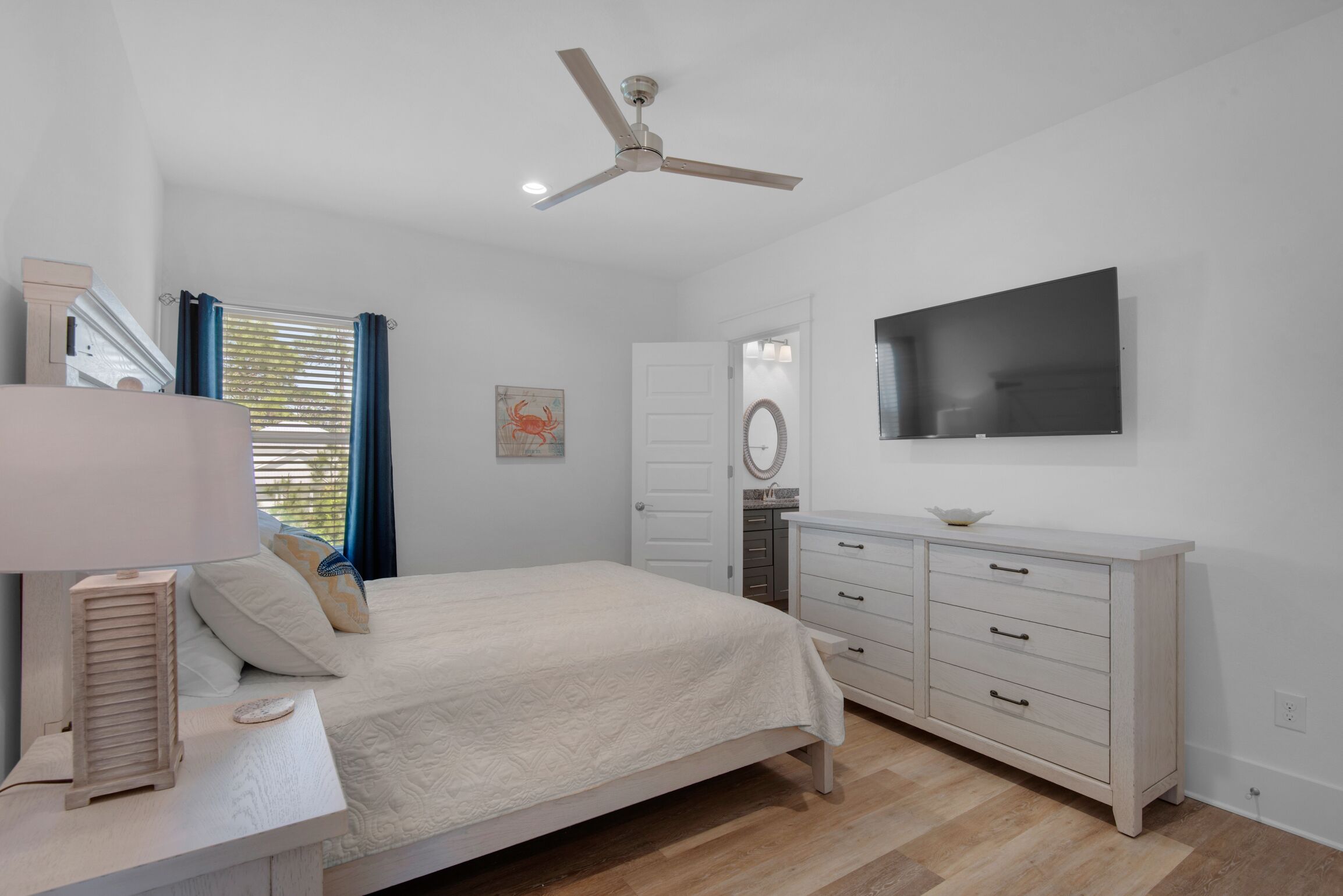 A bedroom with a bed, a dresser, a ceiling fan, a TV, and a window with curtains.