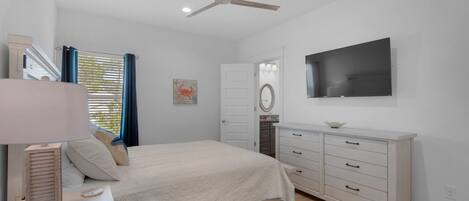A bedroom with a bed, a dresser, a ceiling fan, a TV, and a window with curtains.