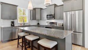 A modern kitchen with grey cabinets, stainless steel appliances, a granite countertop, and bar stools.