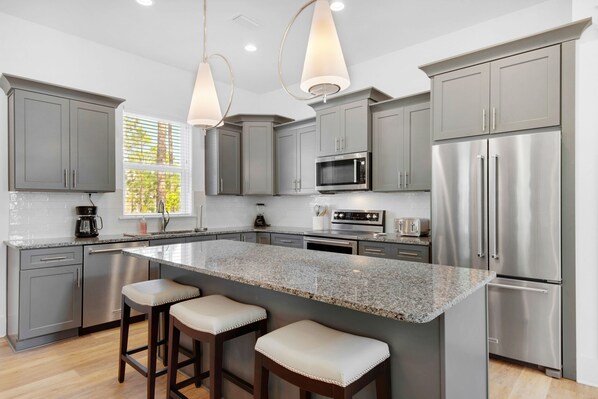 A modern kitchen with grey cabinets, stainless steel appliances, a granite countertop, and bar stools.