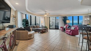 A spacious living room with a large TV, a wooden coffee table, a sofa, and a red chair. - Lighthouse on the Bay unit 213- 3bed/3bath -Large Pet Friendly Condo- Bay Views! (Orange Beach)