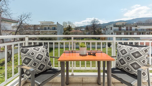 Un balcon avec une table et deux chaises, une plante en pot et une paire de lunettes de soleil posée sur la table.