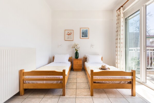 A room with two wooden beds, a nightstand with a vase, and a window with curtains.