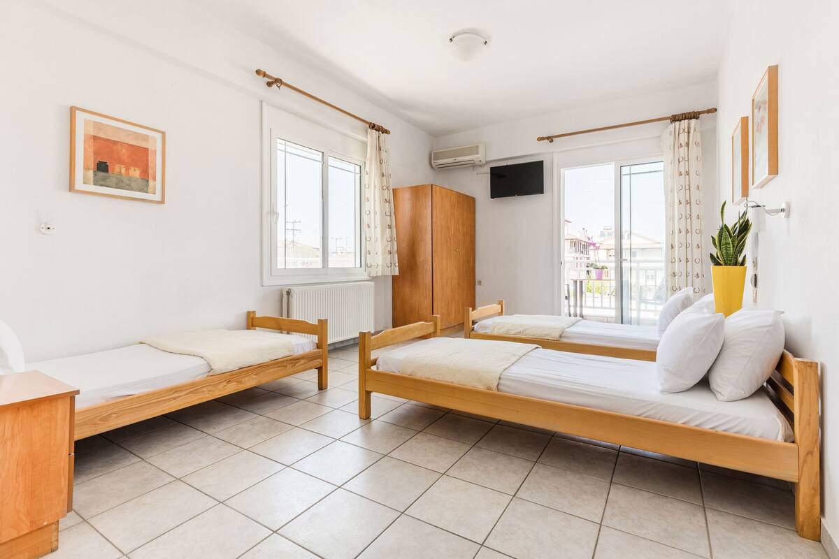 Ein Schlafsaalzimmer mit zwei Holzbetten, einem weißen Heizkörper, einem an der Wand montierten Fernseher und einem Fenster mit Vorhängen.
