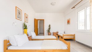 Une pièce avec deux lits en bois, une plante en pot, une petite table et une fenêtre.