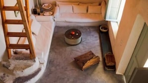 Una habitació acollidora amb una escala de fusta, un sofà, una taula rodona amb una espelma i una petita biblioteca.