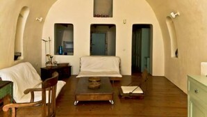 Habitació amb un sostre alt i arquejat, un llit, una taula petita, una cadira i un armari.