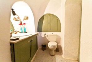 A compact bathroom with a toilet, a sink, and a mirror. - Hanging at the top of the world (Santorini)