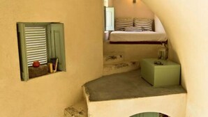 Habitació senzilla amb un llit superposat, una petita estant amb llibres i una olla vermella, i un taulell verd.
