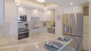 Una cocina moderna con armarios blancos, electrodomésticos de acero inoxidable y encimera de mármol.