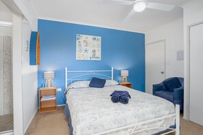 Ein Schlafzimmer mit einem Bett, zwei Nachttischen, einem Deckenventilator, einer blauen Wand und einer Tür.