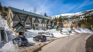 A multi-story lodge with a ski lift visible in the background, surrounded by snow-covered terrain and mountains. - Ski in Ski out at Schweitzer Mountain Resort | Great Views | Cozy Condo (Sandpoint)