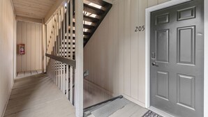 A hallway with a wooden floor, a gray door with the number 205, and a staircase with wooden railings. - Ski in Ski out at Schweitzer Mountain Resort | Great Views | Cozy Condo (Sandpoint)