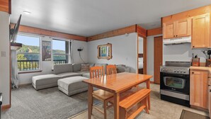 A cozy living area with a sofa, wooden dining table, and kitchen with a stove. - Ski in Ski out at Schweitzer Mountain Resort | Great Views | Cozy Condo (Sandpoint)