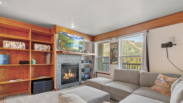 A cozy living room with a fireplace, wooden shelves, a flat-screen TV, and a sofa. - Ski in Ski out at Schweitzer Mountain Resort | Great Views | Cozy Condo (Sandpoint)