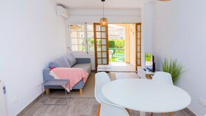 A modern living room with a sofa, a round table, and chairs. There is a TV and a plant in the room. - Isla Saint Tropez Apartment Javea Arenal, with Pool, Wifi, AC and recently Refurbished (Javea / Xàbia)