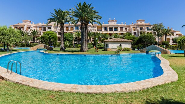 A swimming pool surrounded by palm trees and a building with multiple balconies. - Isla Saint Tropez Apartment Javea Arenal, with Pool, Wifi, AC and recently Refurbished (Javea / Xàbia)