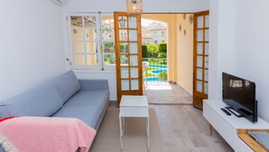 A modern living room with a sofa, a small table, a TV, and a view of a swimming pool through an open door. - Isla Saint Tropez Apartment Javea Arenal, with Pool, Wifi, AC and recently Refurbished (Javea / Xàbia)