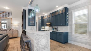Una cocina moderna con armarios azul oscuro, una isla blanca con taburetes altos y luminarias colgantes.