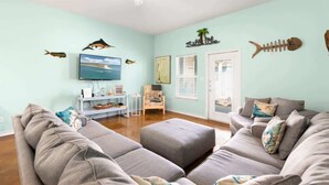 Un salon avec un canapé gris, un téléviseur et des éléments de décoration murale, notamment des motifs de poissons.