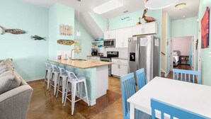 Une cuisine moderne avec des meubles blancs, un îlot central doté de tabourets, un réfrigérateur et un four à micro-ondes.