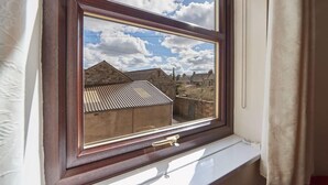 Una ventana con vista a un edificio de techos inclinados y pared de ladrillo.