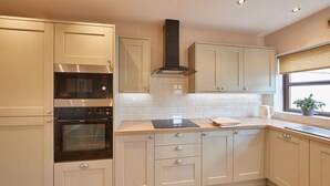 Una cocina moderna con armarios blancos, horno empotrado, microondas y campana extractora.