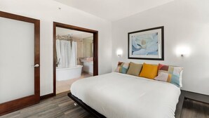 A bedroom with a bed, a framed picture, and a bathroom visible through an open door.
