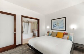 Quarto com cama, um quadro emoldurado e banheiro visível por uma porta aberta.