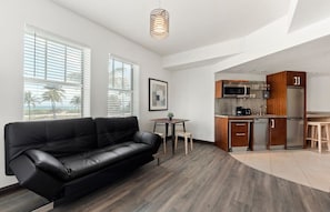 Uma sala de estar moderna com um sofá de couro preto, uma pequena mesa de jantar e uma área de cozinha com armários de madeira e eletrodomésticos de aço inoxidável.