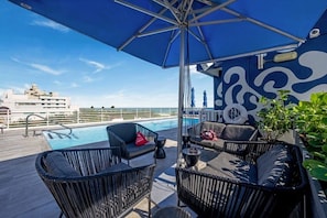 Área de piscina no terraço, com espreguiçadeiras e um grande guarda-sol.