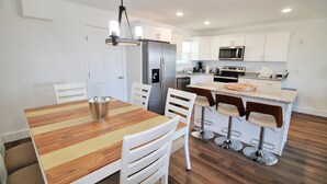 A modern kitchen with white cabinets, a stainless steel refrigerator, a microwave, and a granite countertop. - SHORE BEATS WORK IS 500 STEPS TO BEACH! MODERN, IMMACULATE TOWNHOME! (Mexico Beach)