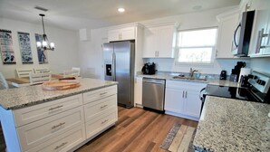 A modern kitchen with white cabinetry, granite countertops, stainless steel appliances, and a wooden floor. - SHORE BEATS WORK IS 500 STEPS TO BEACH! MODERN, IMMACULATE TOWNHOME! (Mexico Beach)