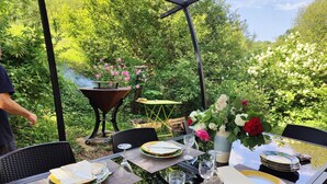 Un espacio al aire libre para comer con una parrilla, mesas, sillas y vistas a zonas verdes.