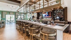 Zona de bar con taburetes, una pantalla de televisión y una barra repleta de botellas.