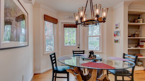 A dining area with a glass table surrounded by chairs, a wooden tree stump centerpiece, and a chandelier.