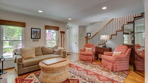 A spacious living room with a beige sofa, patterned armchairs, a wooden coffee table, and a staircase leading to another level.