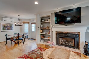 A spacious living room with a fireplace, a dining area with a table and chairs, and a large flat-screen TV mounted above the fireplace.