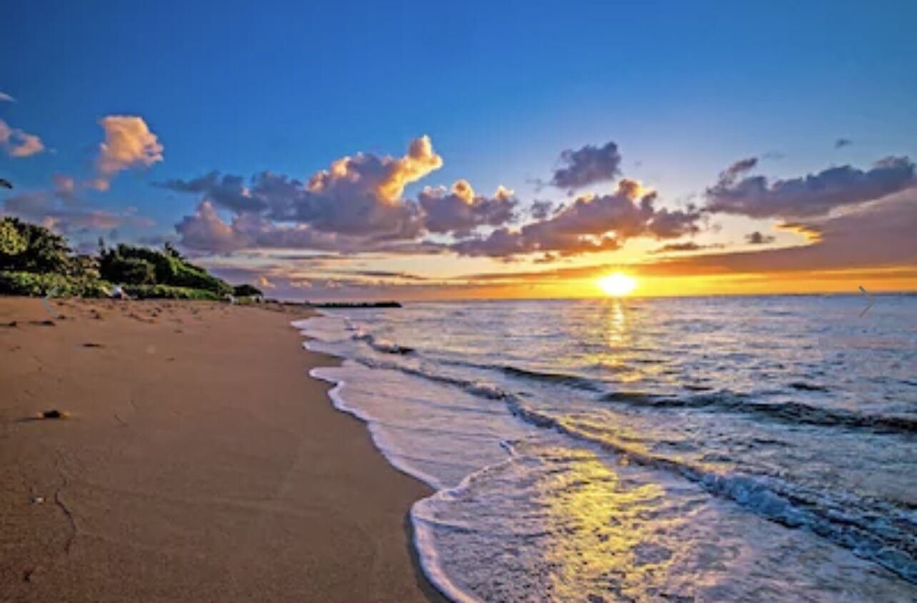 A beach with a sunset over the ocean, clear skies, and a calm sea.