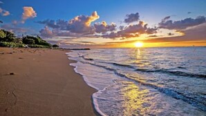 A beach with a sunset over the ocean, clear skies, and a calm sea.