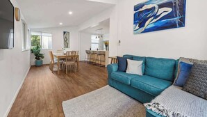 Een ruime woonkamer met een blauwgroene bank, een eettafel en een schilderij aan de muur.