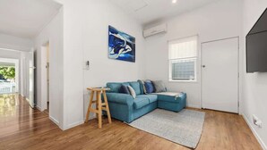 Een moderne woonkamer met een blauwe modulaire bank, een houten krukje, een schilderij en een groot raam.