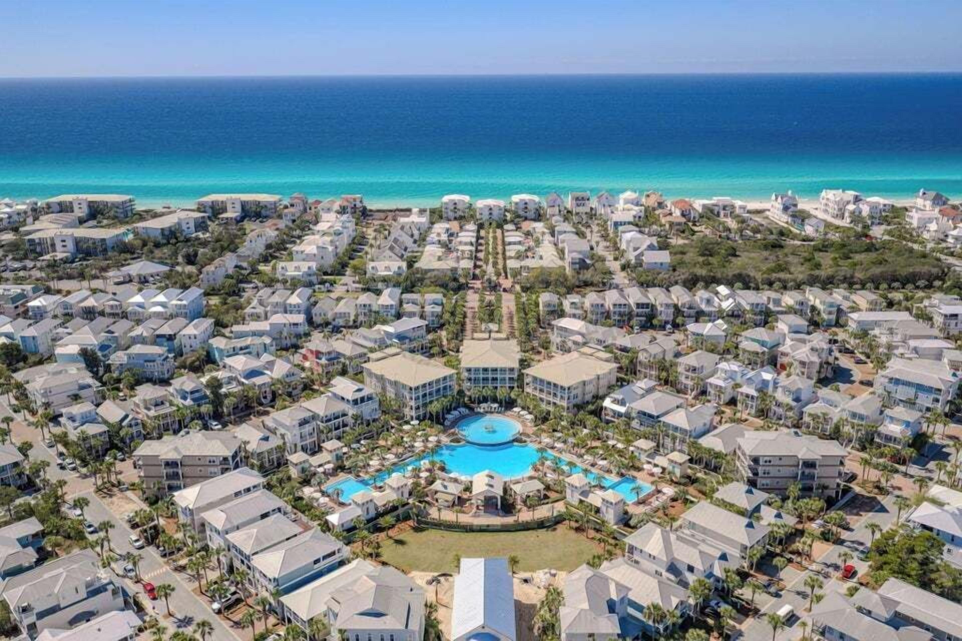 A resort with multiple buildings, a central pool, and a view of the ocean.