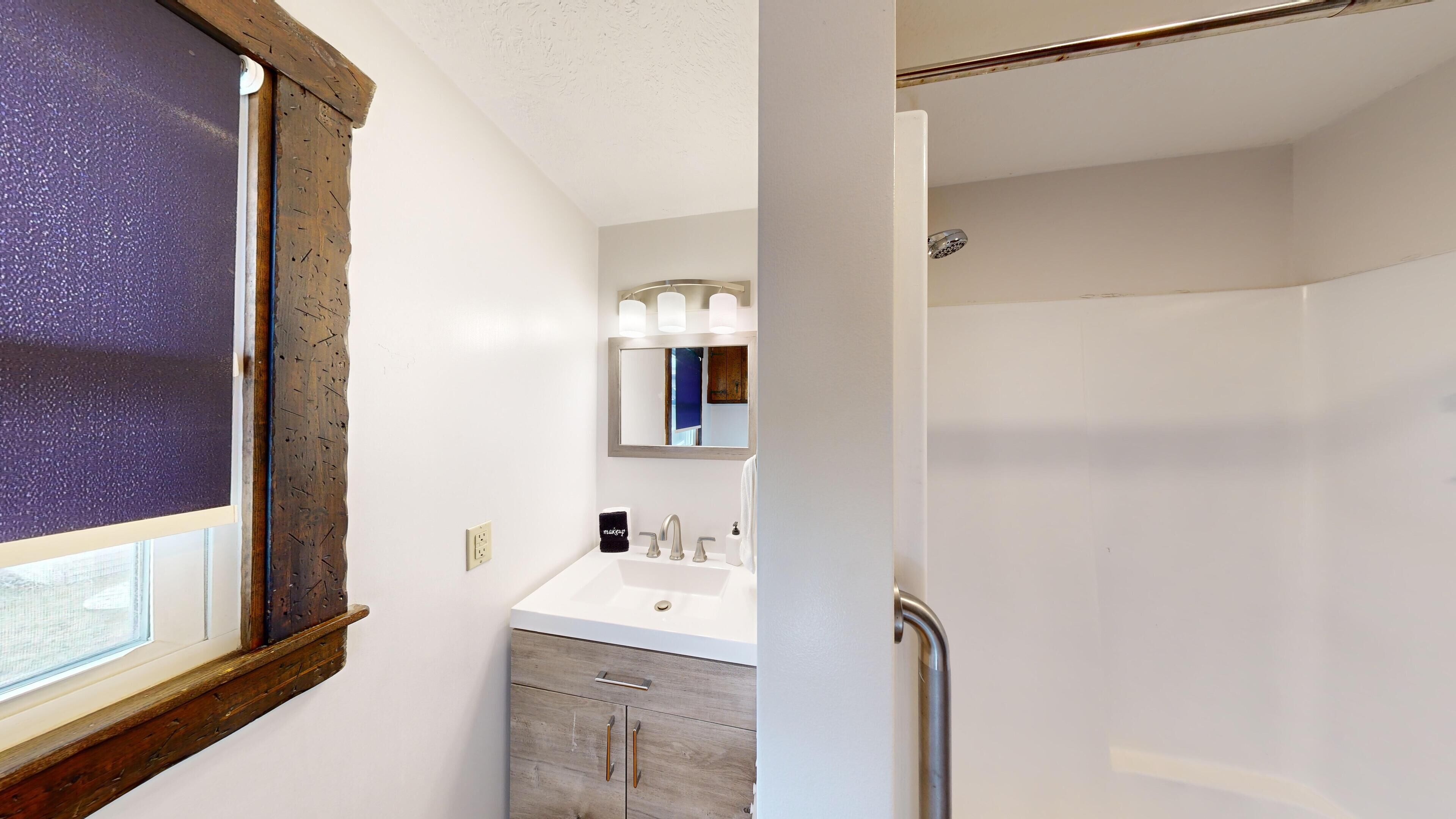A bathroom with a white sink, a mirror, and a shower.