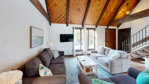 Amplia sala de estar con techo de madera alto, televisor de pantalla plana, dos sofás, una mesa de centro y una escalera que conduce a otro nivel.