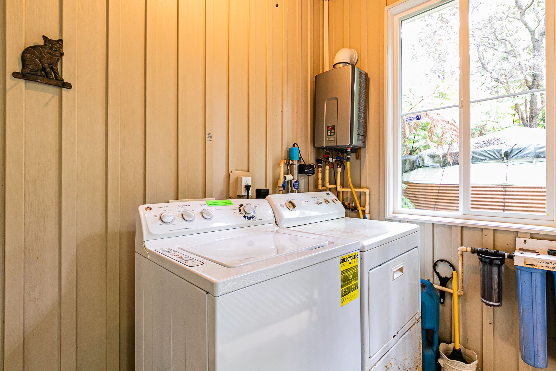 Une buanderie équipée d’un lave-linge et d’un sèche-linge à chargement frontal, d’un chauffe-eau et d’une fenêtre donnant sur l’extérieur.