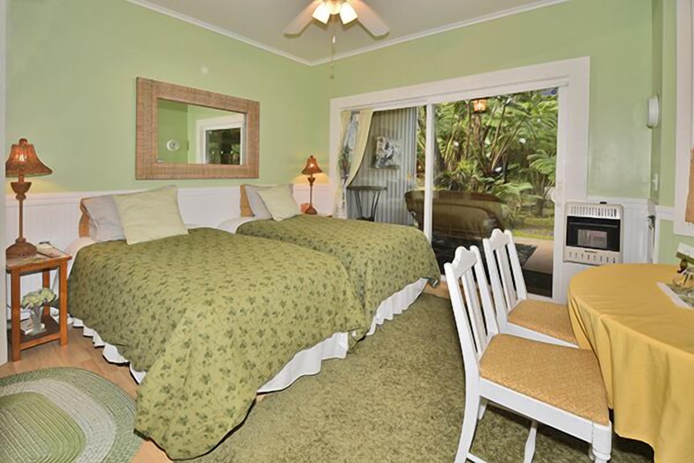 A bedroom with two beds, a chair, a table, a mirror, and a sliding glass door leading to a balcony.