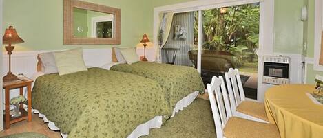 A bedroom with two beds, a chair, a table, a mirror, and a sliding glass door leading to a balcony.