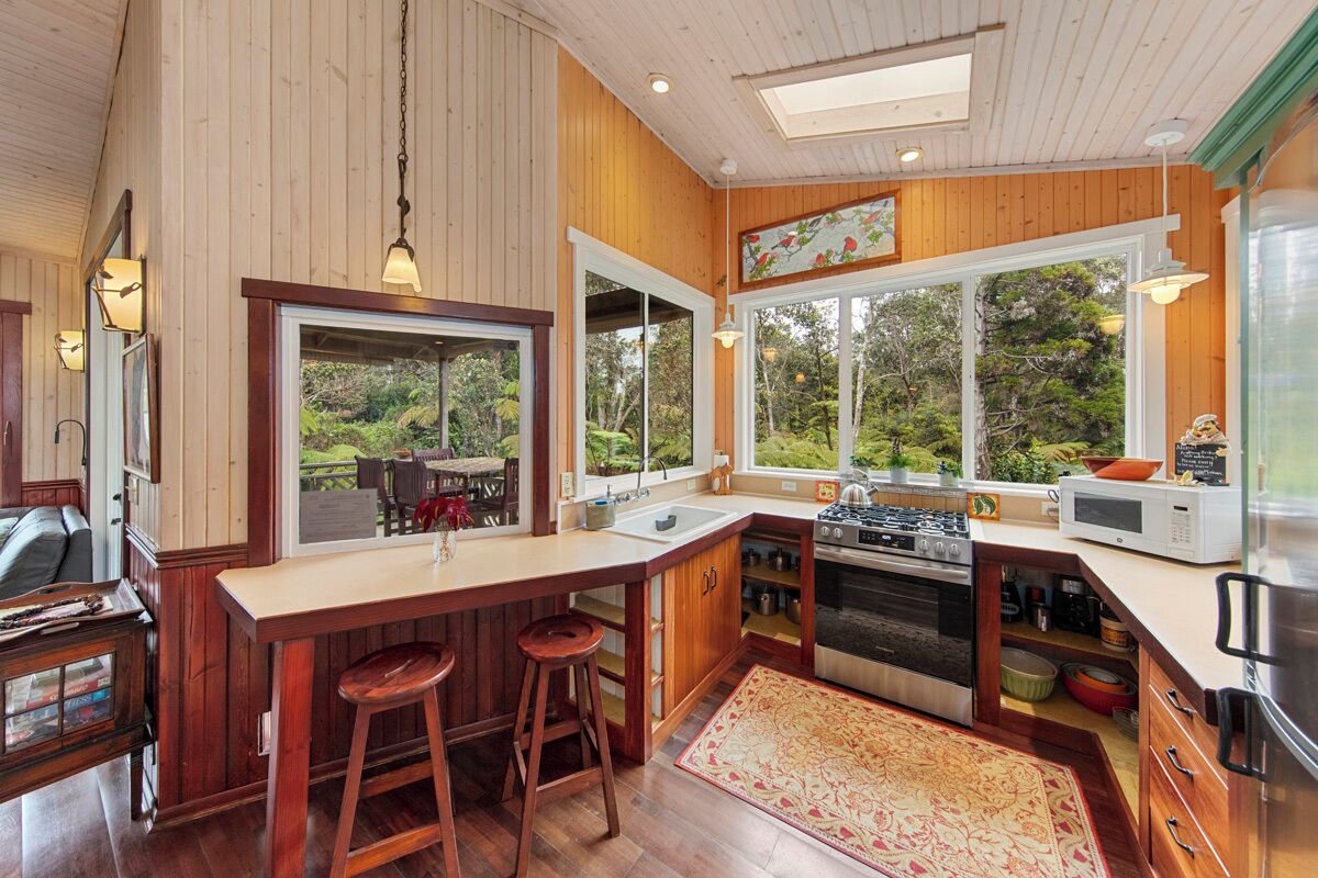 A kitchen with wooden walls, a central island with stools, a large window, and a view of greenery.